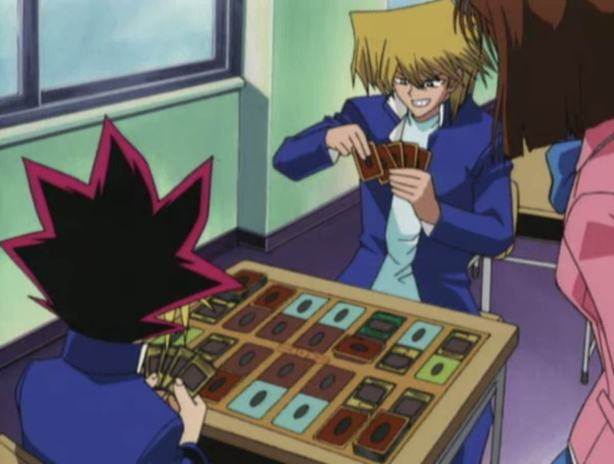 Joey seleziona una carta su un tavolo di carte Yu-Gi-Oh mentre gioca a Yugi