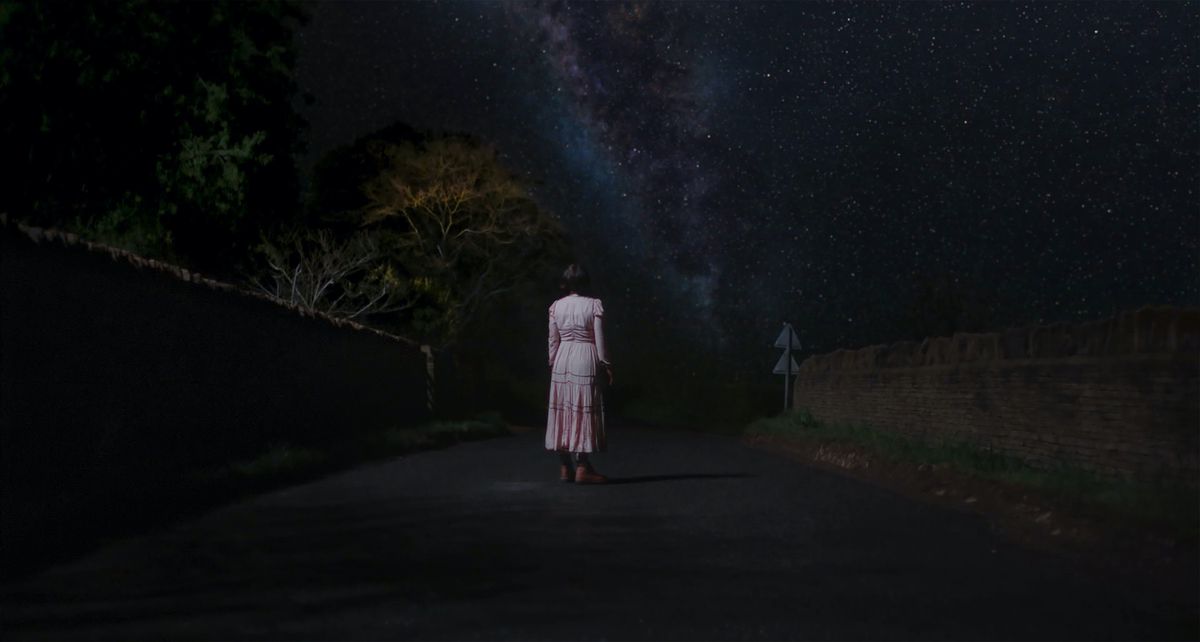 Jessie Buckley, con un lungo vestito rosa, sta fuori di notte sotto un vasto baldacchino di stelle in Men di Alex Garland.