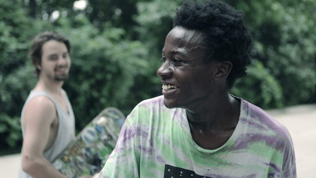 un giovane uomo di colore sorride mentre il suo amico tiene uno skateboard sullo sfondo per badare al divario