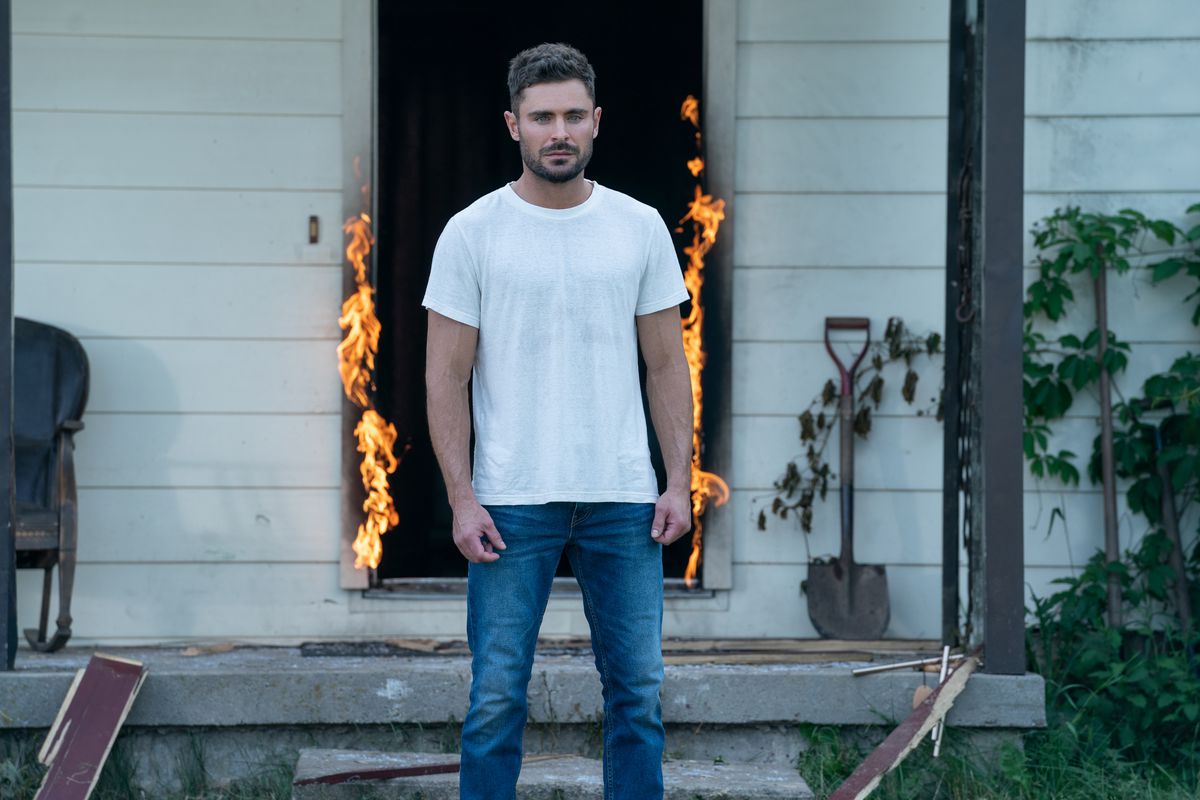 Zac Efron in Firestarter, in piedi fuori davanti a una casa con una porta aperta e in fiamme