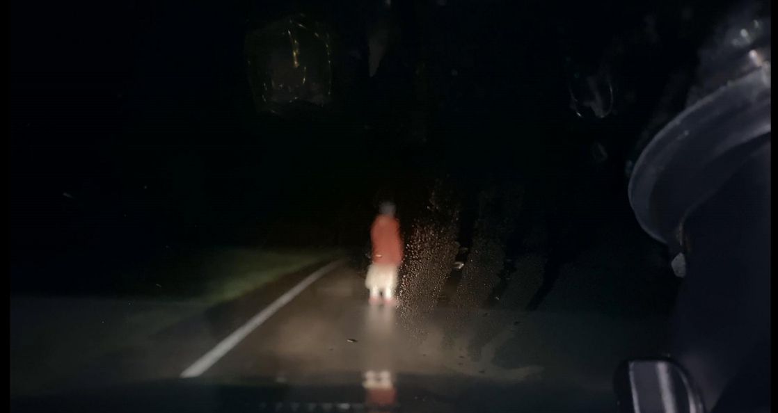 Una donna si trova in mezzo a una strada di notte illuminata dai fari di un'auto in Dashcam.