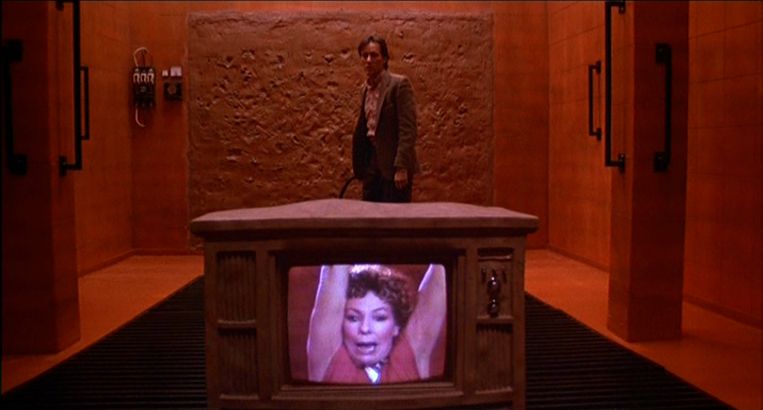 James Woods in una stanza arancione, dietro un televisore che ritrae una donna legata, in Videodrome.