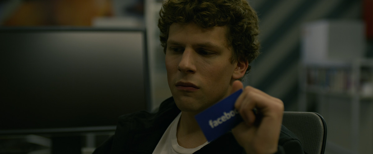 Jesse Eisenberg detiene una carta con il logo di Facebook in The Social Network.