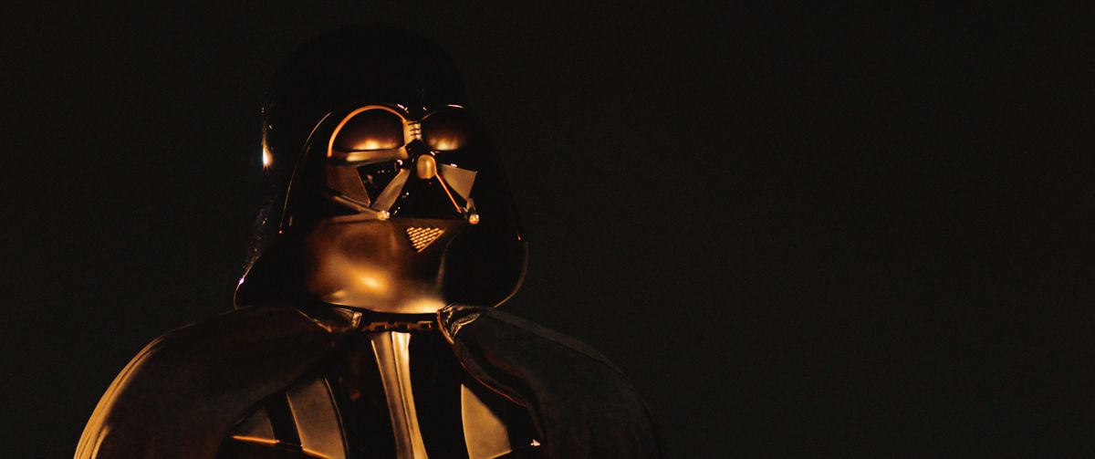 Un Darth Vader (Hayden Christensen) mascherato è illuminato da fiamme su uno sfondo scuro a Obi-Wan Kenobi.