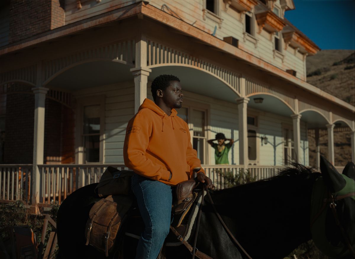 OJ (Daniel Kaluuya), che indossa una felpa con il marchio The Scorpion King arancione, in cima a un cavallo in piedi di fronte a una casa fatiscente, con sua sorella Emerald (Keke Palmer) in piedi sotto il portico, in Nope