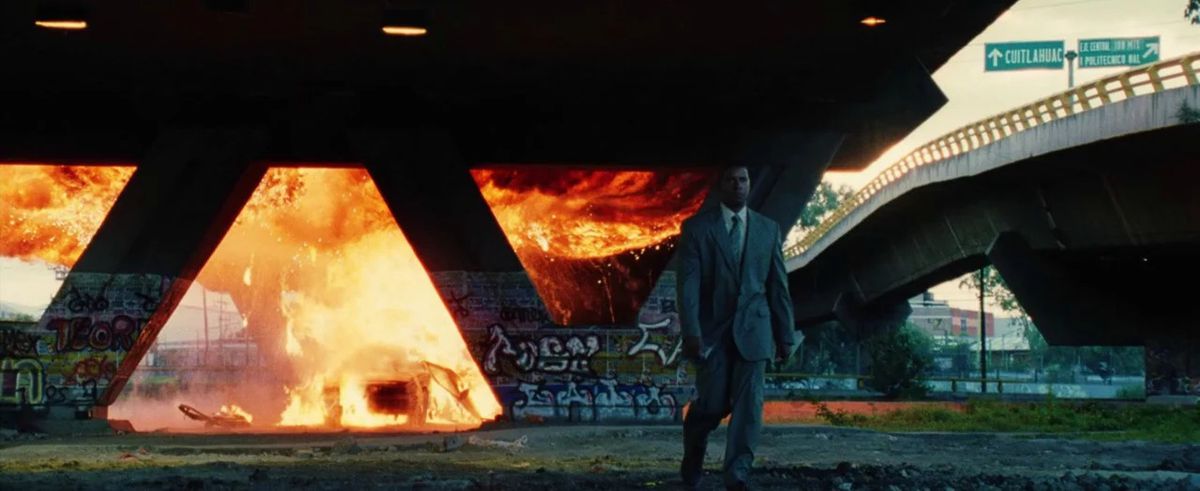 Creasy si allontana da un'auto avvolta dalle fiamme sotto un sottopassaggio autostradale in Man on Fire.