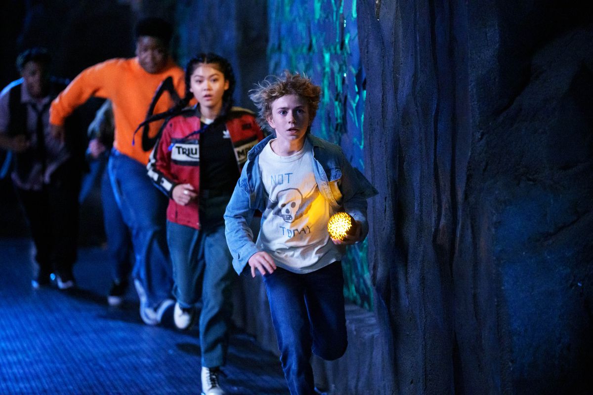 Charlie, un ragazzo biondo, guida un gruppo di bambini attraverso un corridoio buio