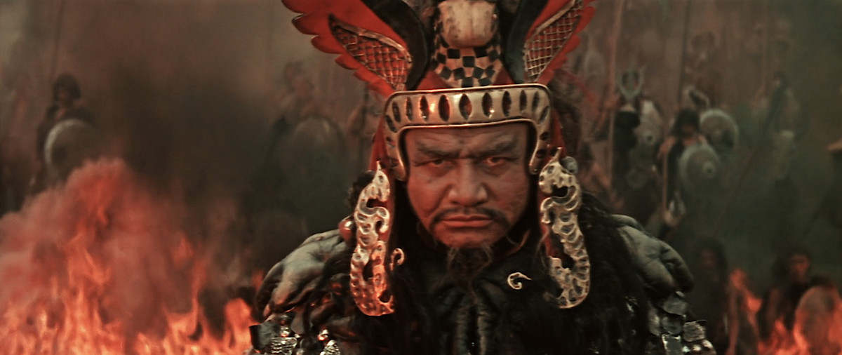 Un guerriero in primo piano con un vivace copricapo rosso e oro nel mezzo di un'ardente battaglia a Ilya Muromets