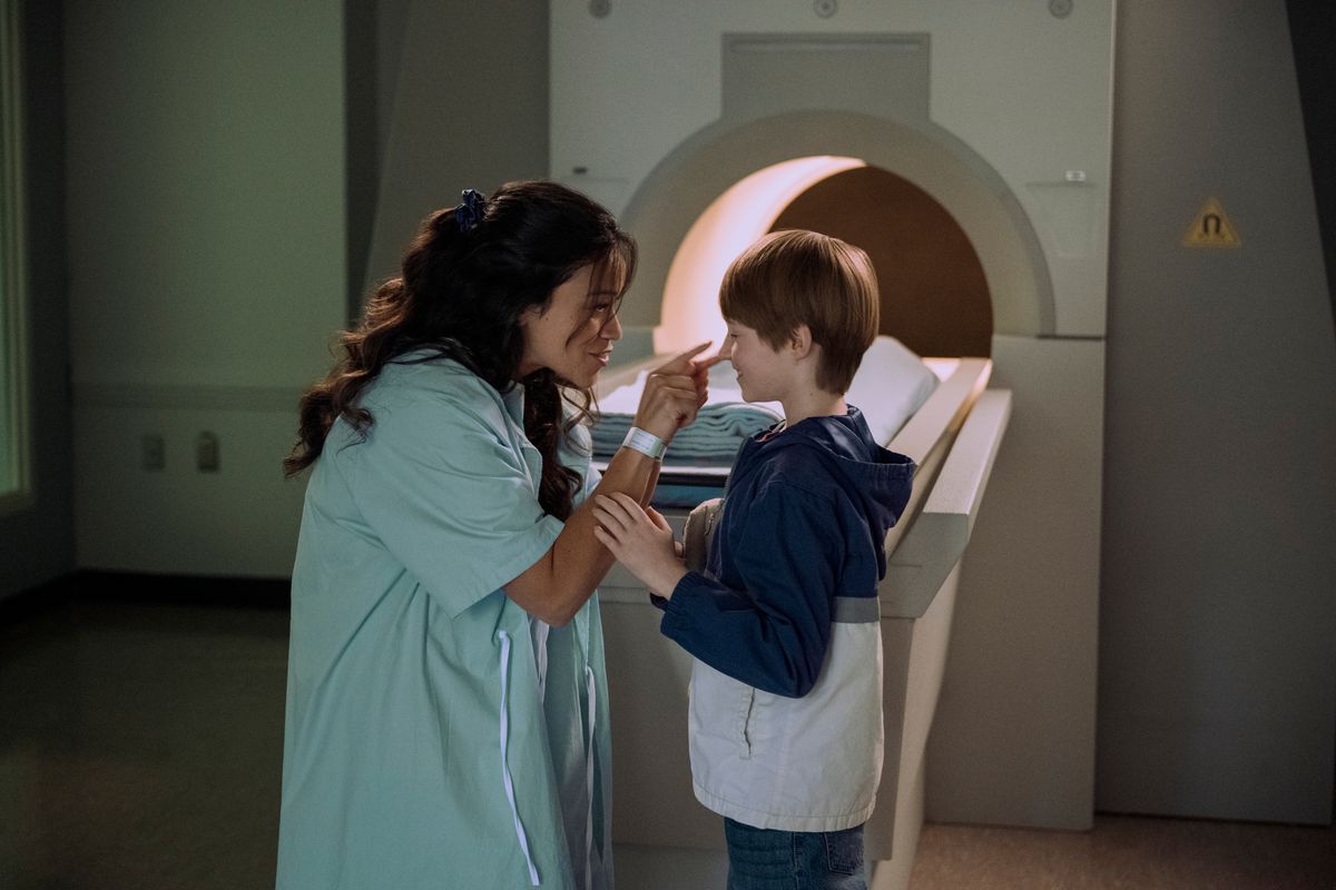 gina rodriguez indossa un camice da ospedale, sporgendosi per toccare il naso di un ragazzino, mentre è davanti a una risonanza magnetica