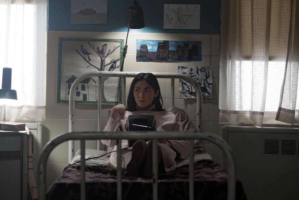 Isabelle Fuhrman nel ruolo di Esther in Orphan: First Kill seduta su un letto a leggere un libro