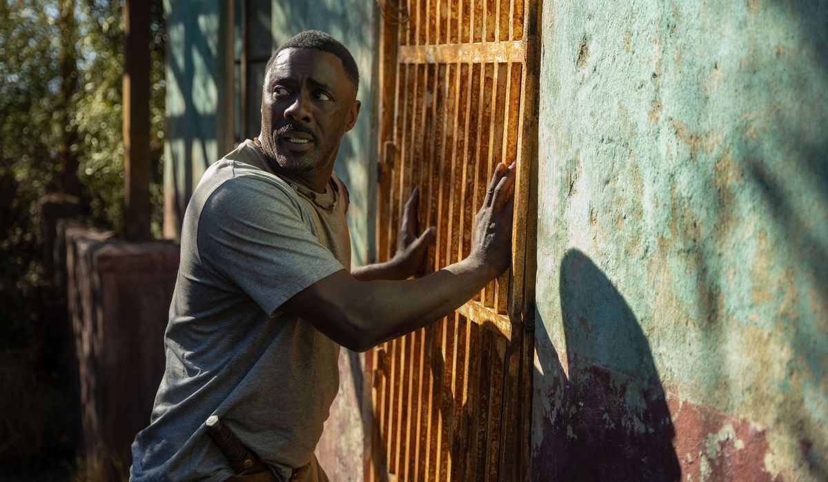 Idris Elba è in piedi contro una porta esterna chiusa a chiave e arrugginita, guardando nervosamente alle sue spalle in Bestia