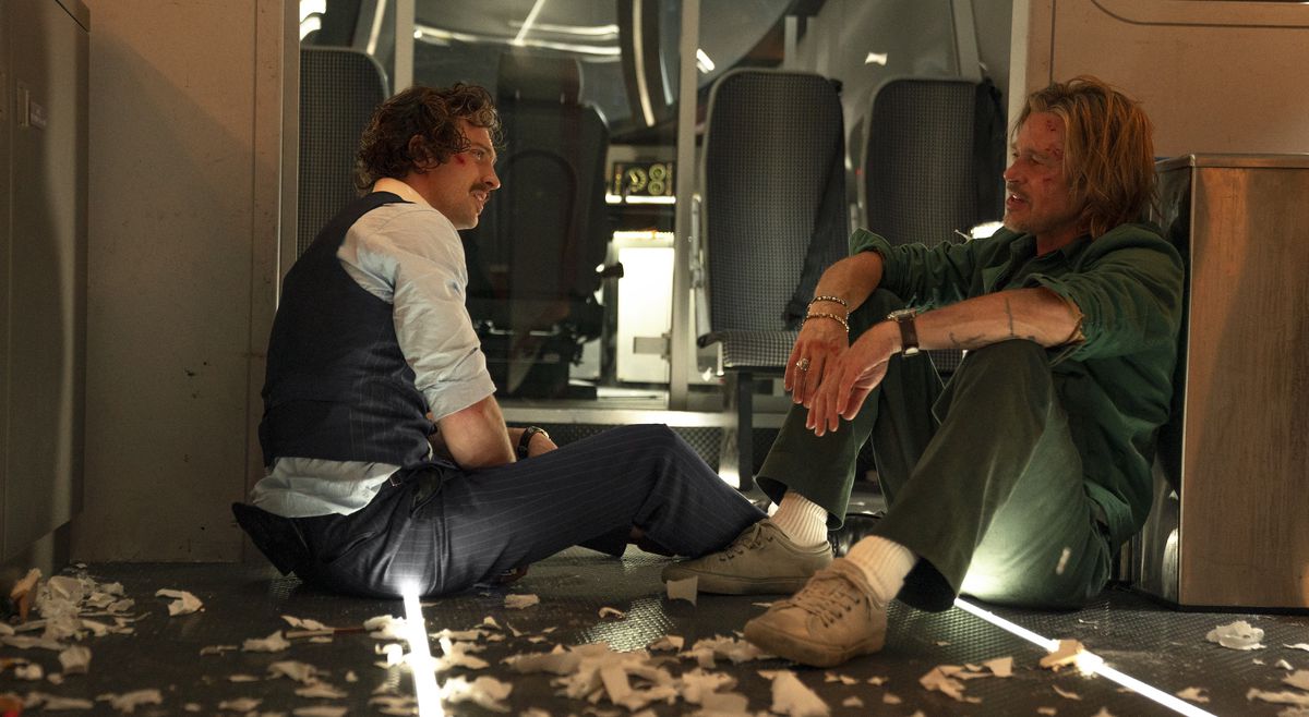 Aaron Taylor-Johnson e Brad Pitt, insanguinati e sporchi, condividono un momento seduti in mezzo a mucchi di carta strappata in Bullet Train