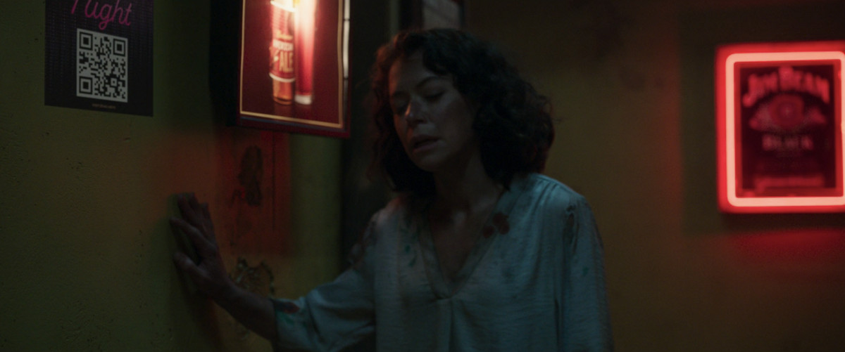 Una Jen Walters (She-Hulk, interpretata da Tatiana Maslany) inzuppata di sangue si appoggia a un muro in un bar di She-Hulk.  C'è un adesivo sul muro con un codice QR visibile. 