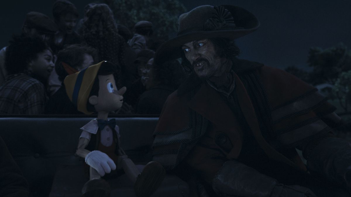 Luke Evans nei panni del cocchiere siede al posto di guida del suo pullman accanto a un curioso Pinocchio in CG nel remake live-action della Disney del suo classico animato del 1940
