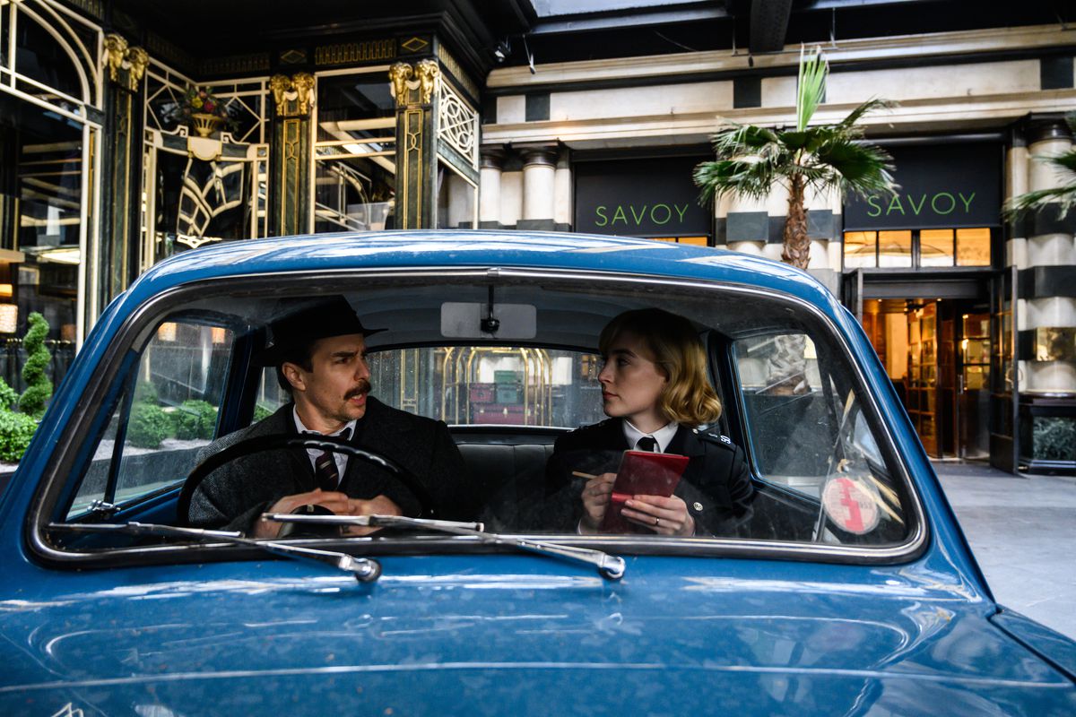 L'ispettore Stoppard (Sam Rockwell) e l'agente Stalker (Saoirse Ronan) parlano in una piccola macchina blu della polizia fuori dal Savoy Hotel