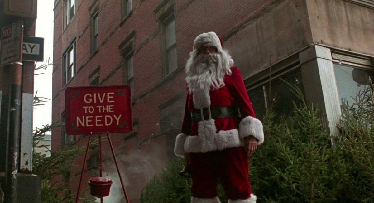 Un uomo vestito da Babbo Natale si trova di fronte a un edificio in mattoni e un cartello rosso che dice 
