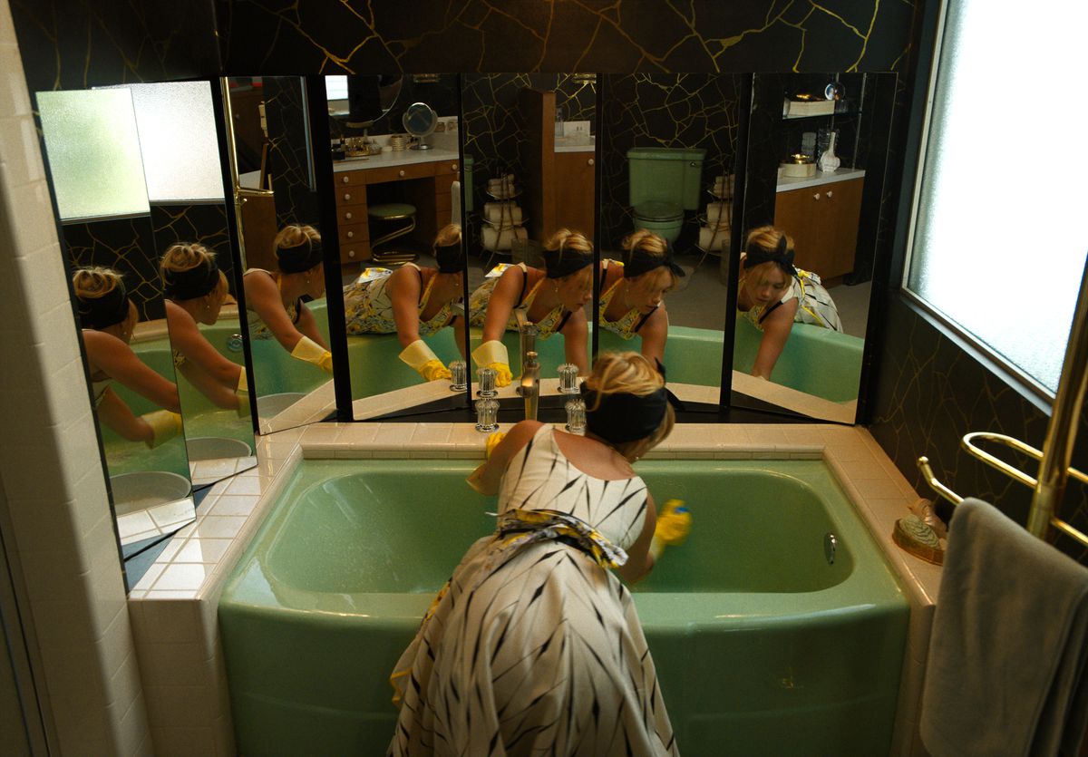Florence Pugh nei panni di Alice strofina una vasca da bagno verde con un grazioso vestito anni '50.  Ci dà le spalle e vediamo il suo riflesso rifratto in una serie di specchi