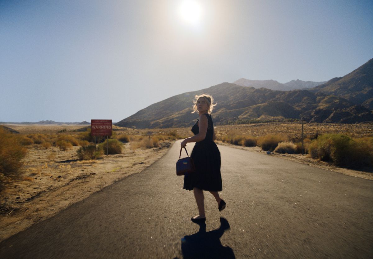 Florence Pugh nei panni di Alince percorre una strada deserta verso il sole, voltandosi a guardare alle sue spalle.  Indossa un vestito nero e porta una borsetta