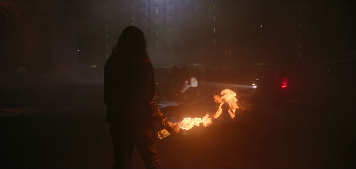 Una figura stagliata con in mano una molotov fiammeggiante si trova per le strade di Parigi ad Athena
