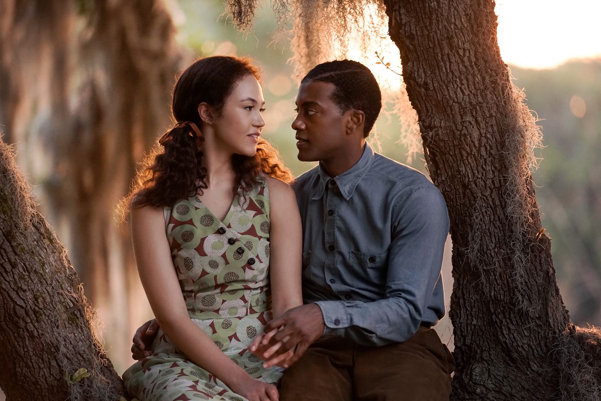 Una coppia seduta su un albero, una con una camicia abbottonata e una con un vestito, si guardano negli occhi.