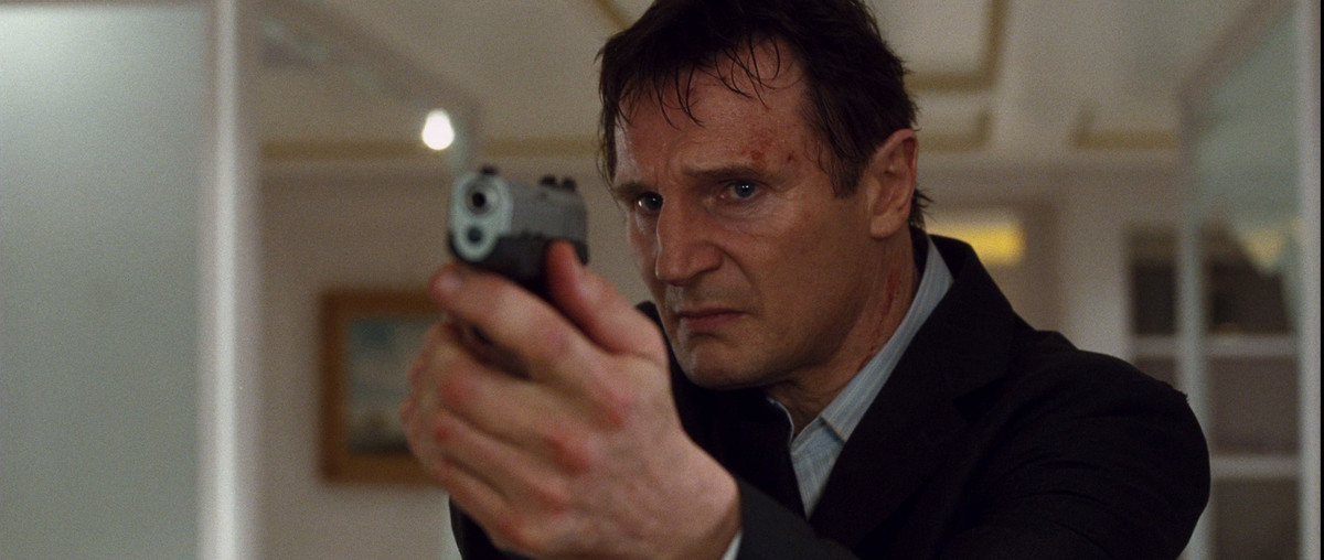 Liam Neeson indossa un abito e tiene una pistola verso la telecamera in Taken