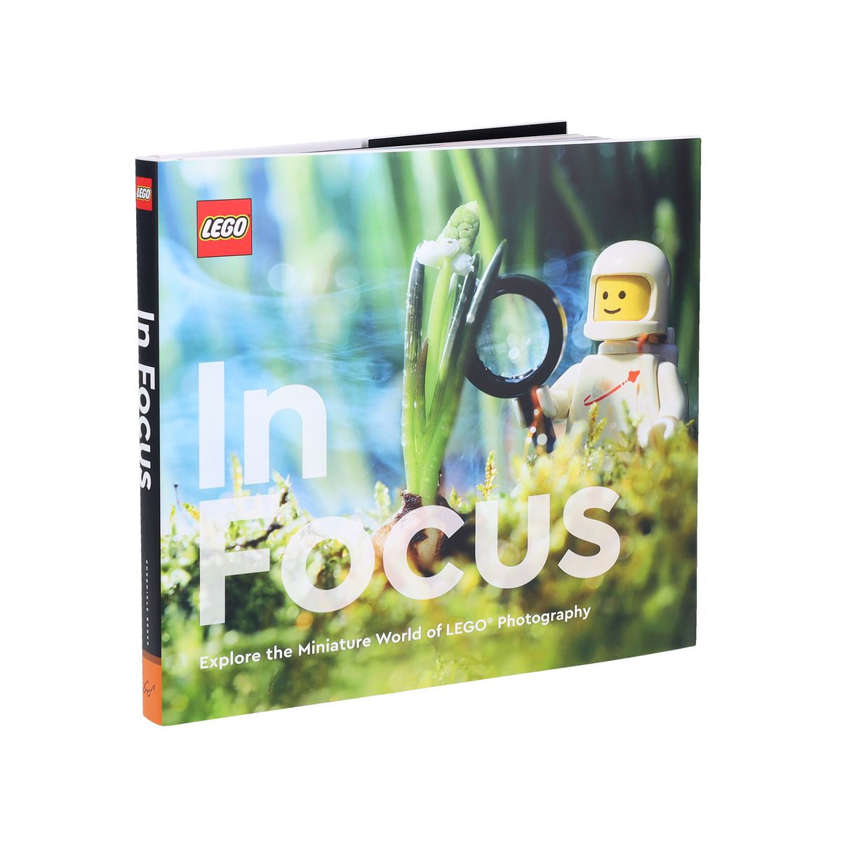 La copertina di Lego in Focus, con un elmetto spaziale che indossa un uomo in bianco con in mano una lente d'ingrandimento che guarda una piccola pianta