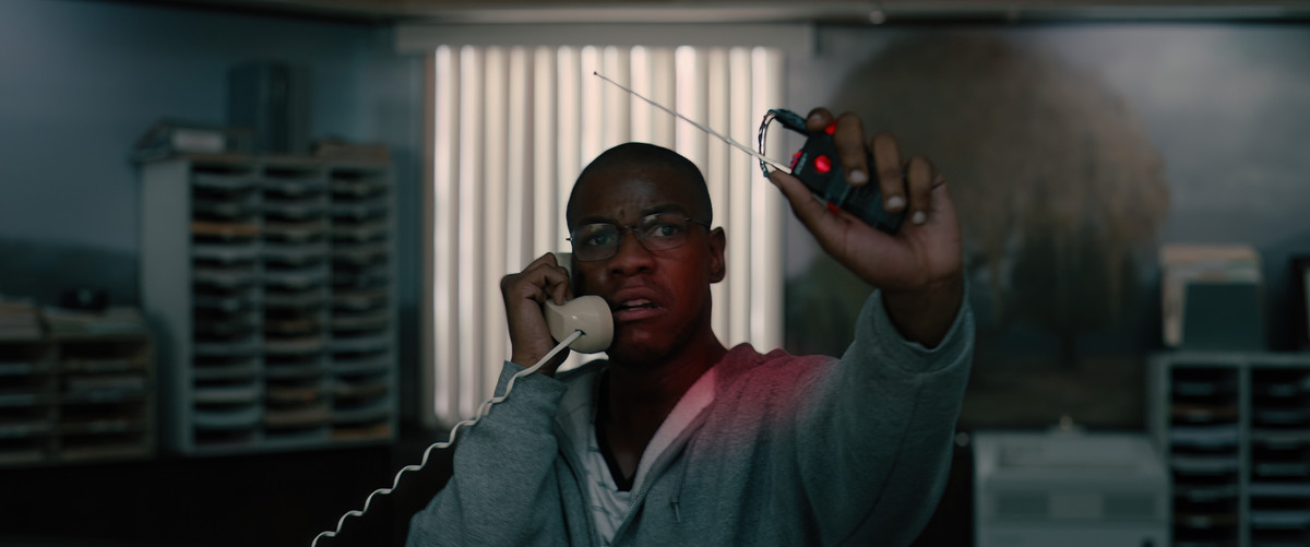 John Boyega indossa una felpa con cappuccio grigia e tiene un detonatore in una mano mentre è al telefono nell'altra in Breaking.