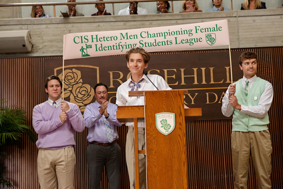un ragazzo biondo magro davanti a uno striscione che dice cis etero uomini che difendono la lega delle studentesse che identificano le donne.  dietro di lui, tre uomini applaudono