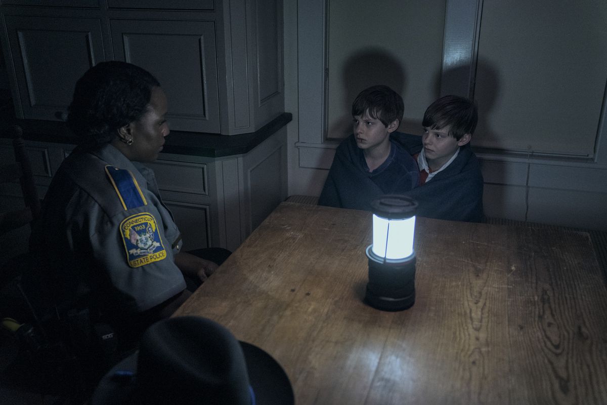 Una poliziotta nera parla con i gemelli Elias e Lucas in una stanza poco illuminata illuminata da una vivida lanterna nel film Goodnight Mommy del 2022