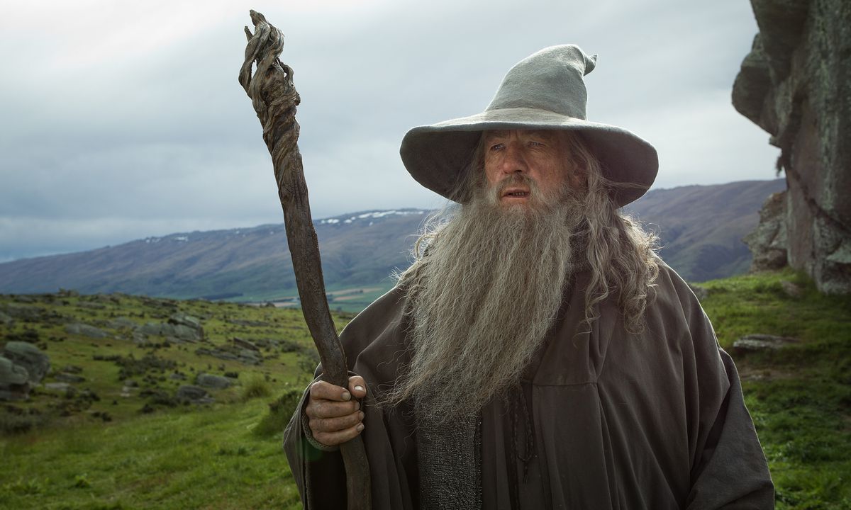 Gandalf il Grigio tiene il suo bastone con un campo verdeggiante e collinare dietro di lui in Lo Hobbit: Un Viaggio Inaspettato