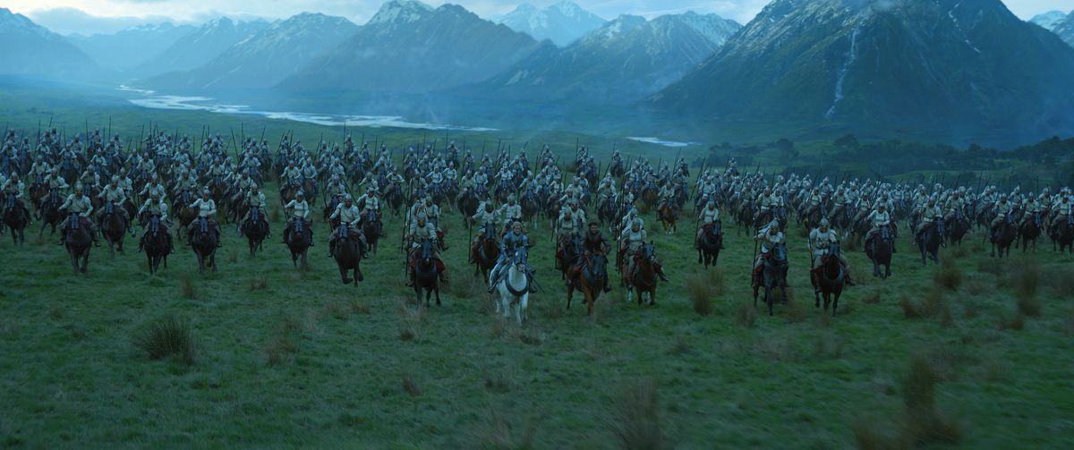 Galadriel cavalca con le forze Numenoriane attraverso un campo panoramico, con montagne e un fiume sullo sfondo dietro di loro 