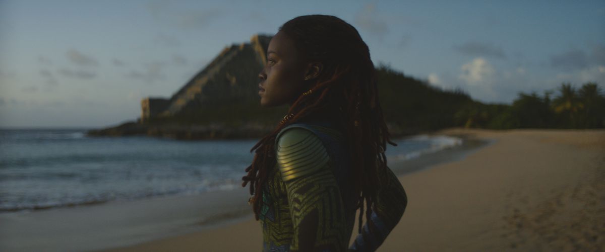 Lupita Nyong'O nei panni di Nakia, in piedi su una spiaggia che guarda verso l'oceano in Black Panther: Wakanda Forever. 