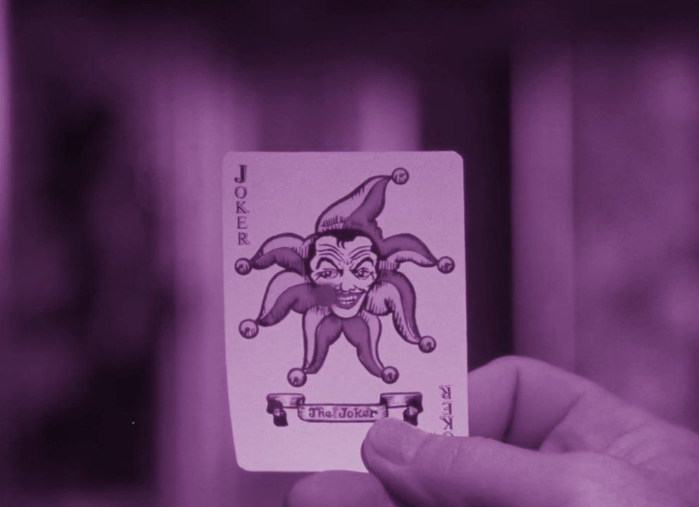 Un fotogramma colorato di viola di un uomo che tiene in mano una carta da gioco Joker in Batman: The Silent Motion Picture.