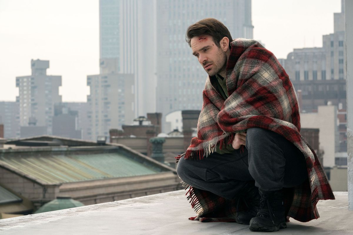Charlie Cox nei panni di Matt Murdock avvolto in una coperta su un tetto con uno squarcio in testa pensando alla vita con New York sullo sfondo