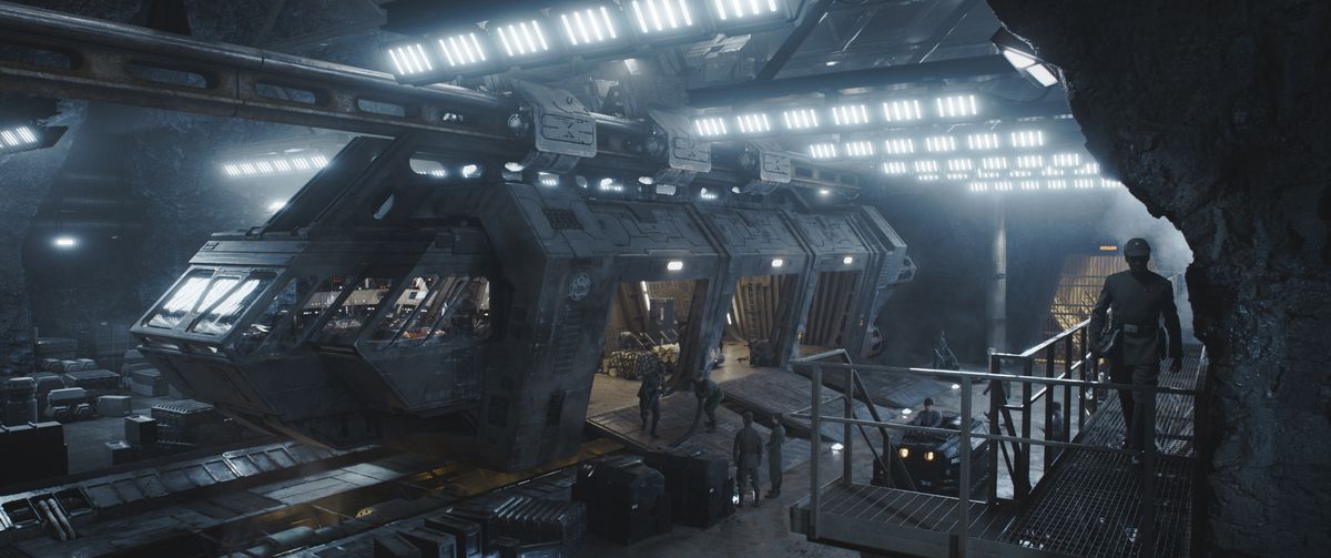 Una nave mercantile che i ribelli stanno per rubare seduta in un hangar imperiale con le rampe di carico aperte mentre un ufficiale cammina su una passerella sopra di essa nell'Andor di Disney Plus.