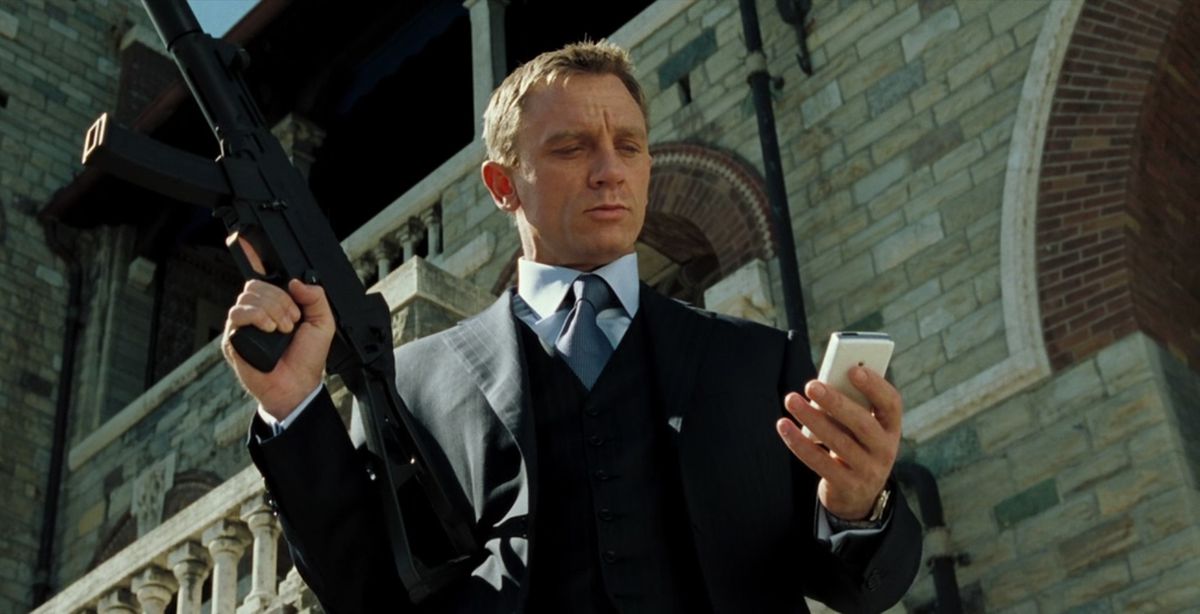 Daniel Craig nei panni di James Bond in Casino Royale, che indossa un abito e controlla il suo telefono mentre impugna una pistola