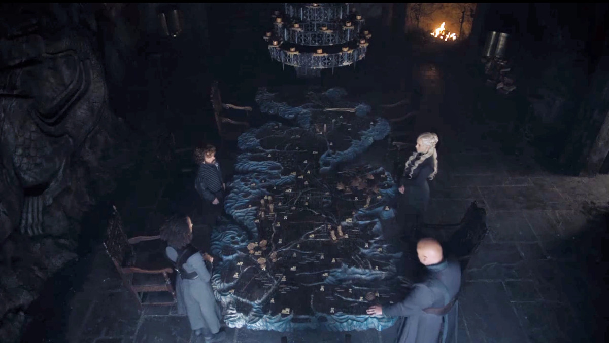 Daenerys Targaryen e i suoi consiglieri stanno attorno al tavolo dipinto (senza luci soffuse) in Il Trono di Spade)