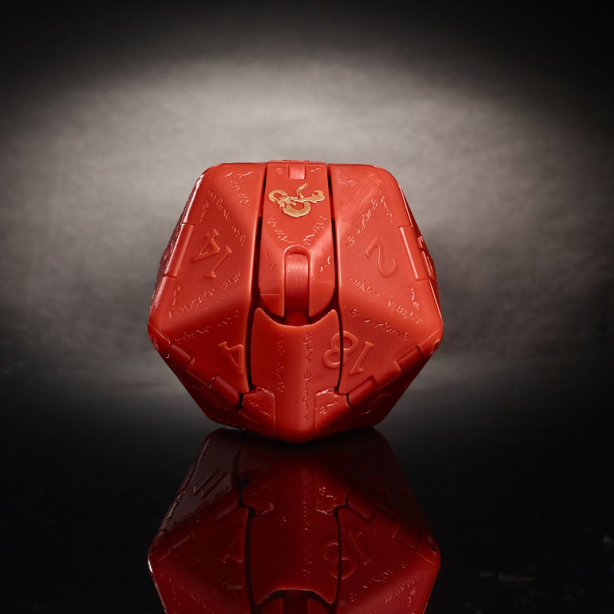 Un drago rosso intrappolato all'interno di un dado a 20 facce.  Una e commerciale dorata luccica nell'illuminazione dello studio.