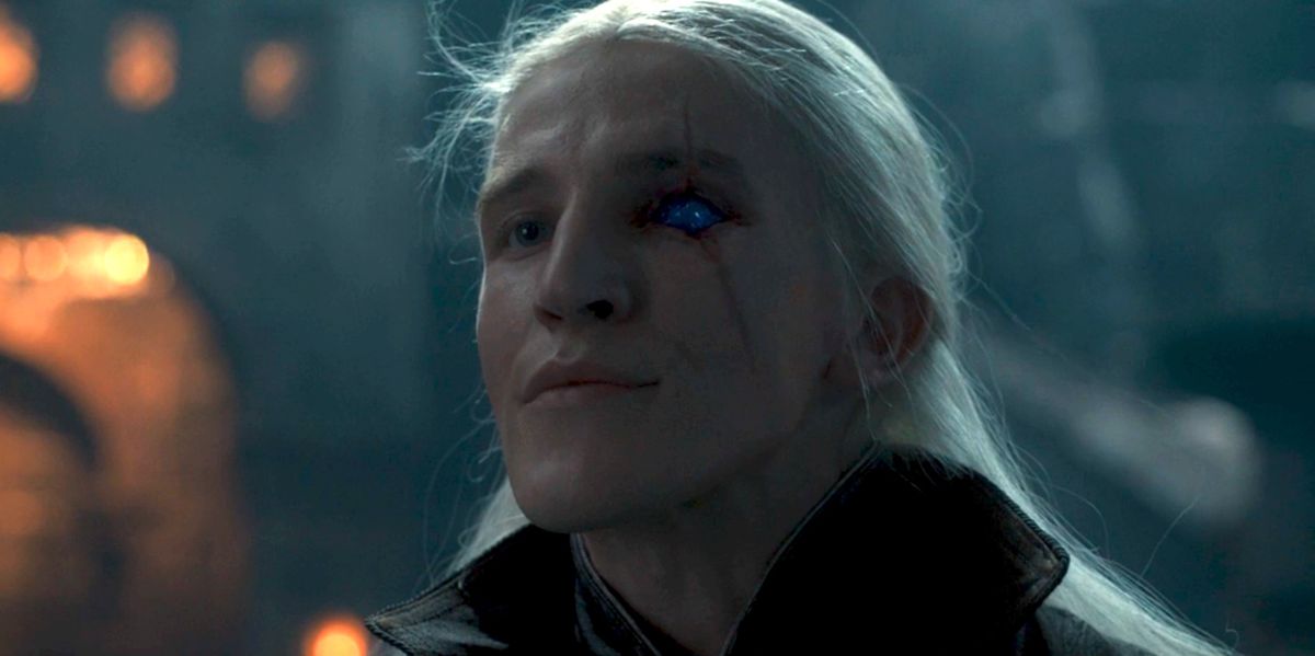 Aemond Targaryen con i capelli bianchi e fruscianti si alza con il mento in alto per rivelare il suo occhio di zaffiro da sotto la benda sull'occhio in La casa del drago