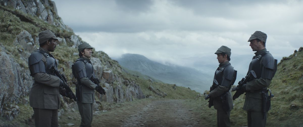 I ribelli (Andor, Tarawyn, Skeen e Nemik) indossano armature nere imperiali mentre sorvegliano un sentiero attraverso la montagna in una giornata nuvolosa nell'Andor di Disney Plus.