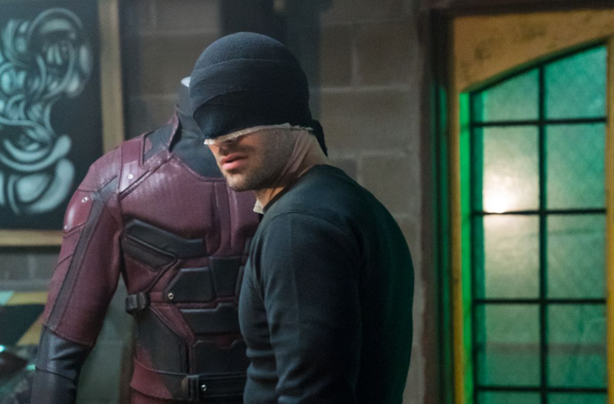 Daredevil (Charlie Cox) nel suo costume da ninja nero guardando il costume da temerario rosso della serie Daredevil del 2015.