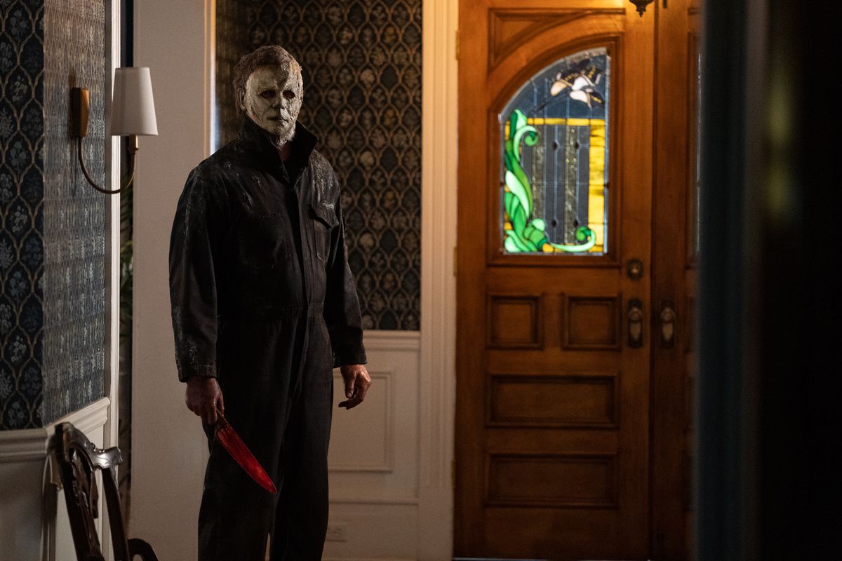 Michael Myers con la sua maschera bianca sfilacciata tiene un coltello insanguinato nell'atrio di una casa rustica a Halloween Ends