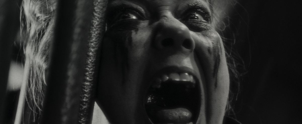 Verussa (Harriet Sansom Harris), viso striato di trucco rituale, urla in primo piano estremo in Werewolf By Night della Marvel