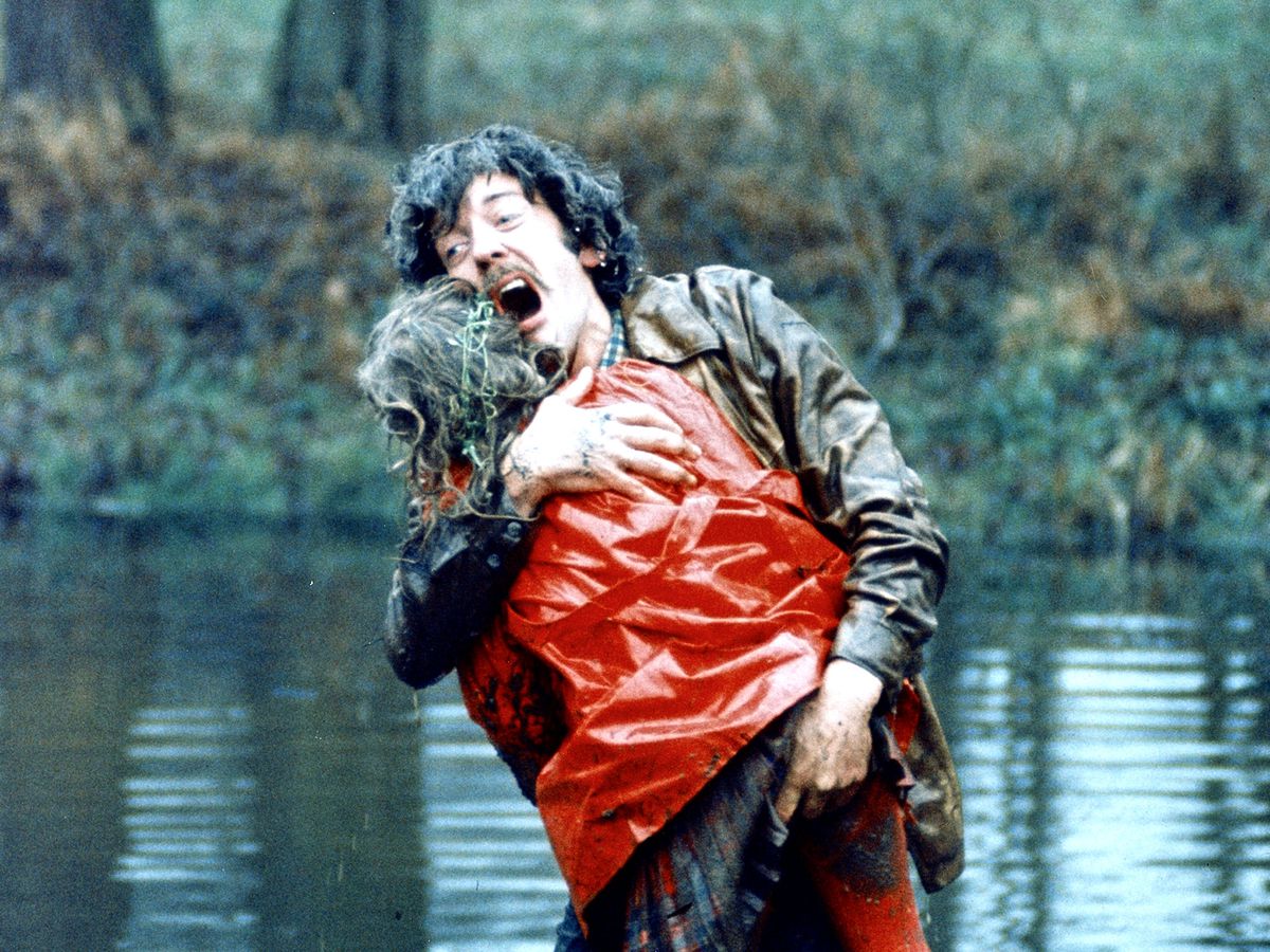 Donald Sutherland urla di dolore mentre tiene una figura senza vita con un impermeabile rosso vicino a un lago in Non guardare ora