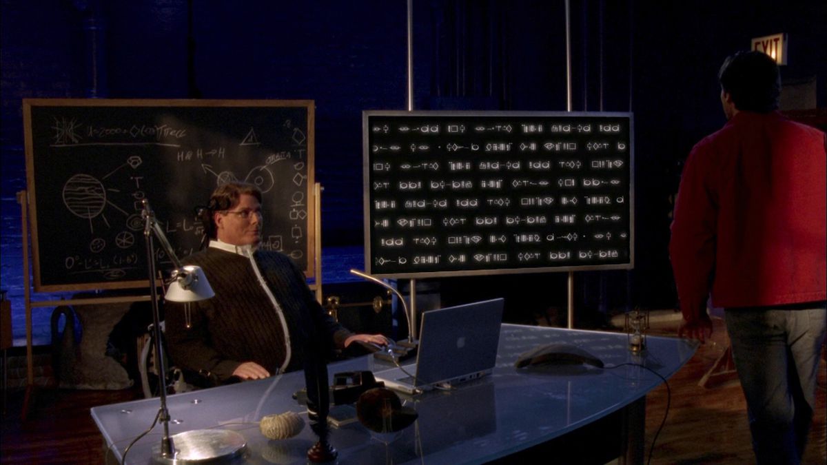 Christopher Reeves nei panni di un personaggio di Smallville seduto a una scrivania con una lavagna e lo schermo di un computer dietro di lui.  Lo schermo del computer ha molto codice e Superman di Tom Welling si sta avvicinando.
