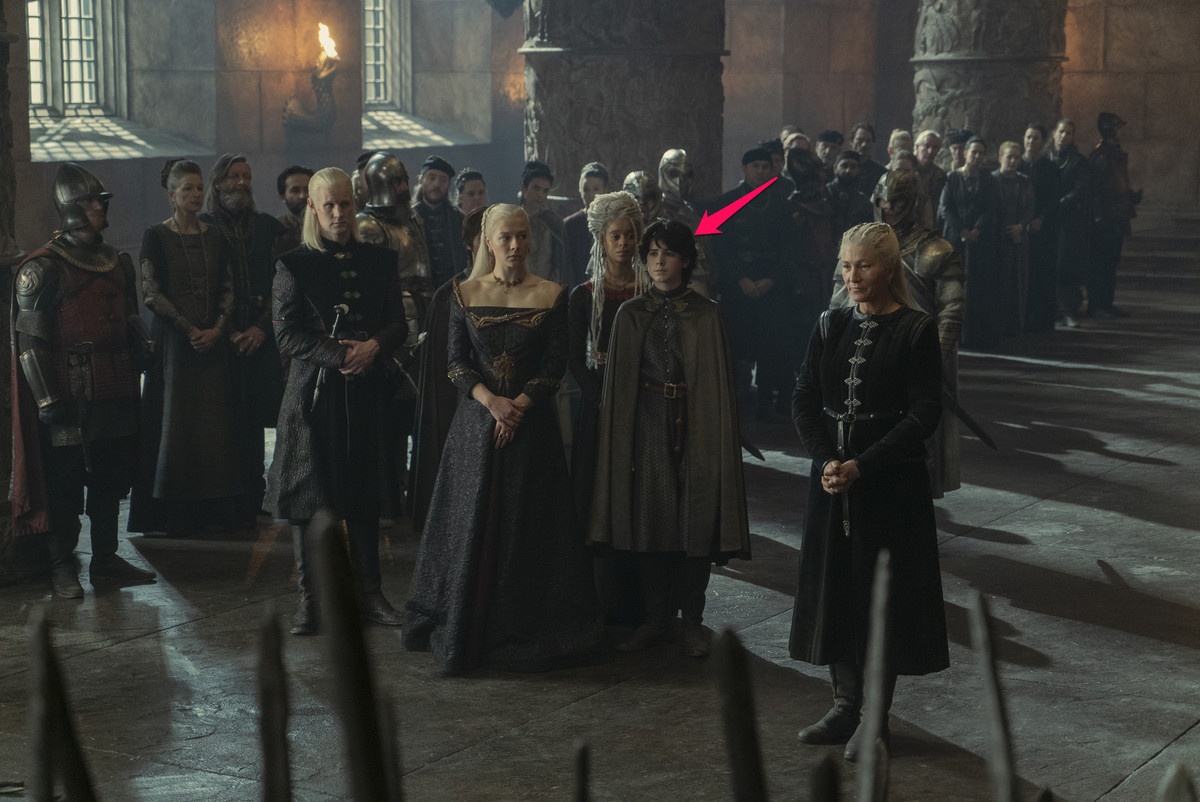 Lucerys Velaryon in piedi con la sua famiglia tra cui Rhaenyra Targaryen, Daemon Targaryen, Rhaena Targaryen e Jacaerys Velaryon nella sala del trono della Fortezza Rossa nella Casa del Drago