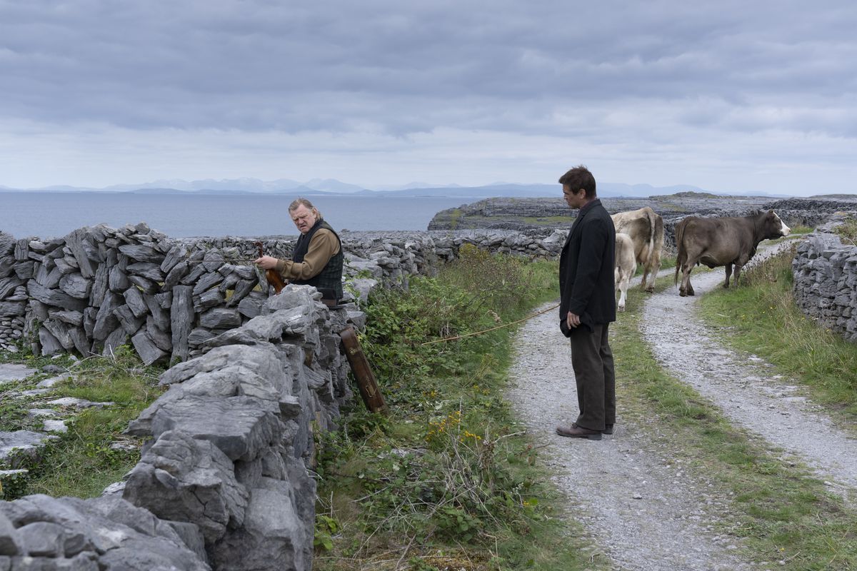 Pádraic (Colin Farrell) cerca di parlare con il suo ex amico Colm (Brendan Gleeson) mentre entrambi gli uomini sono in piedi in una stradina solcata da un carro trainato da un asino, circondati da basse staccionate di pietra, in The Banshees of Inisherin