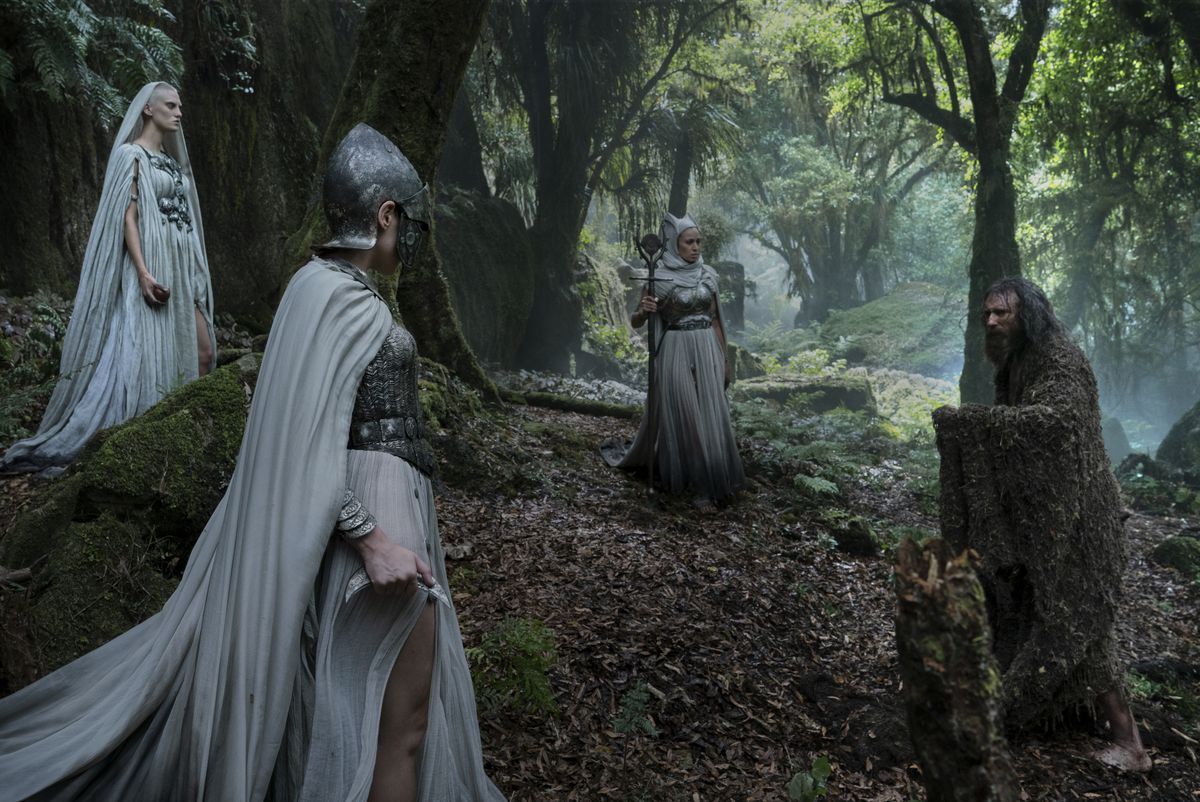 Lo Straniero affronta tre guerrieri dal mantello bianco disposti a triangolo nella foresta in Rings of Power