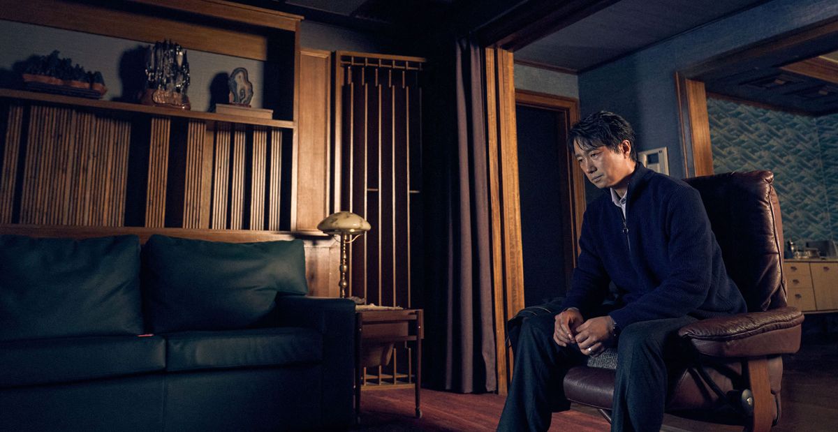 Il detective Hae-jun (Park Hae-il), indossa un abito e sembra esausto, siede da solo in una stanza buia rivestita di intarsi in legno scuro in Decision To Leave