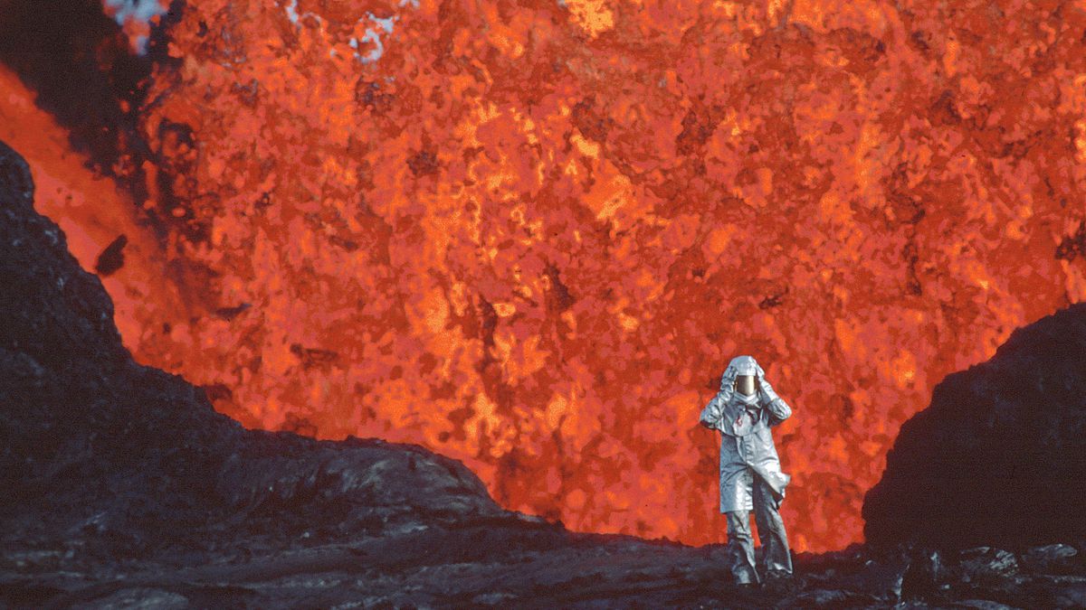 Una persona in tuta ignifuga si allontana dalla bocca del geyser traboccante di lava.